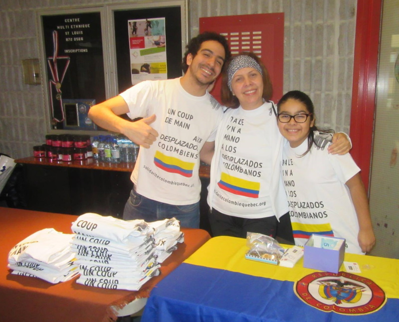 Trois bénévoles vendent des t-shirt indiquant : Un coup de main aux desplazados colombiens.
